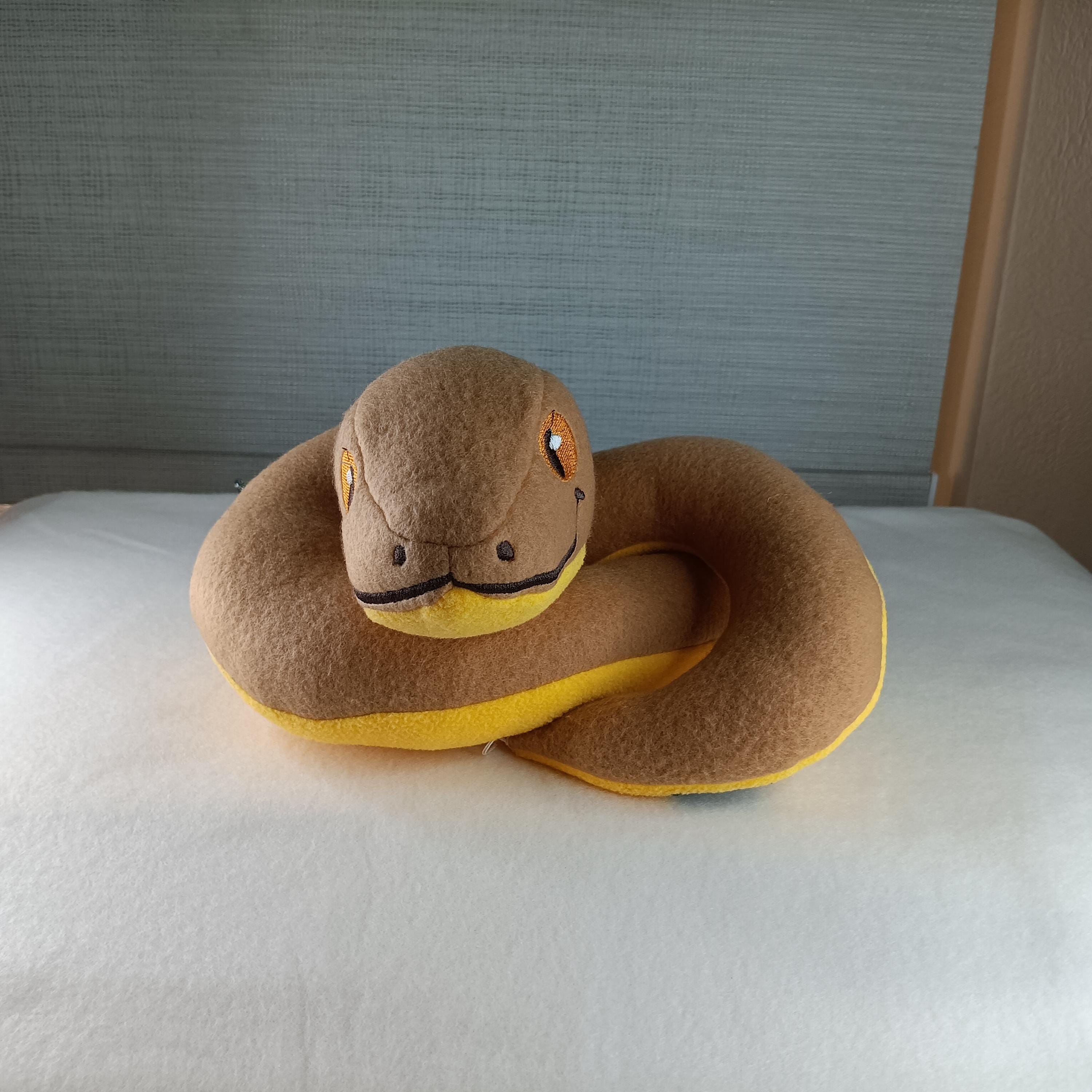 Snake-shaped pillow on a white surface with a neutral background